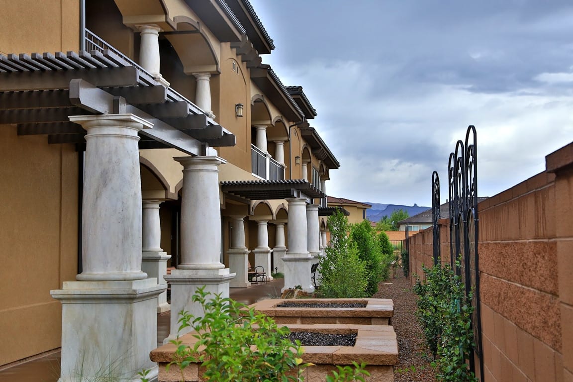 A view of a building with decorative columns and a garden, set against a cloudy sky.