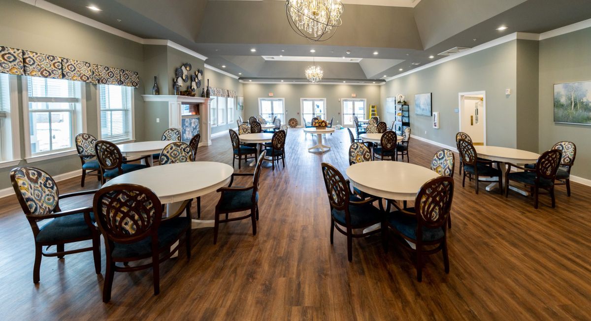 A spacious dining room with elegant chandeliers and wooden floors, featuring several round tables and chairs.