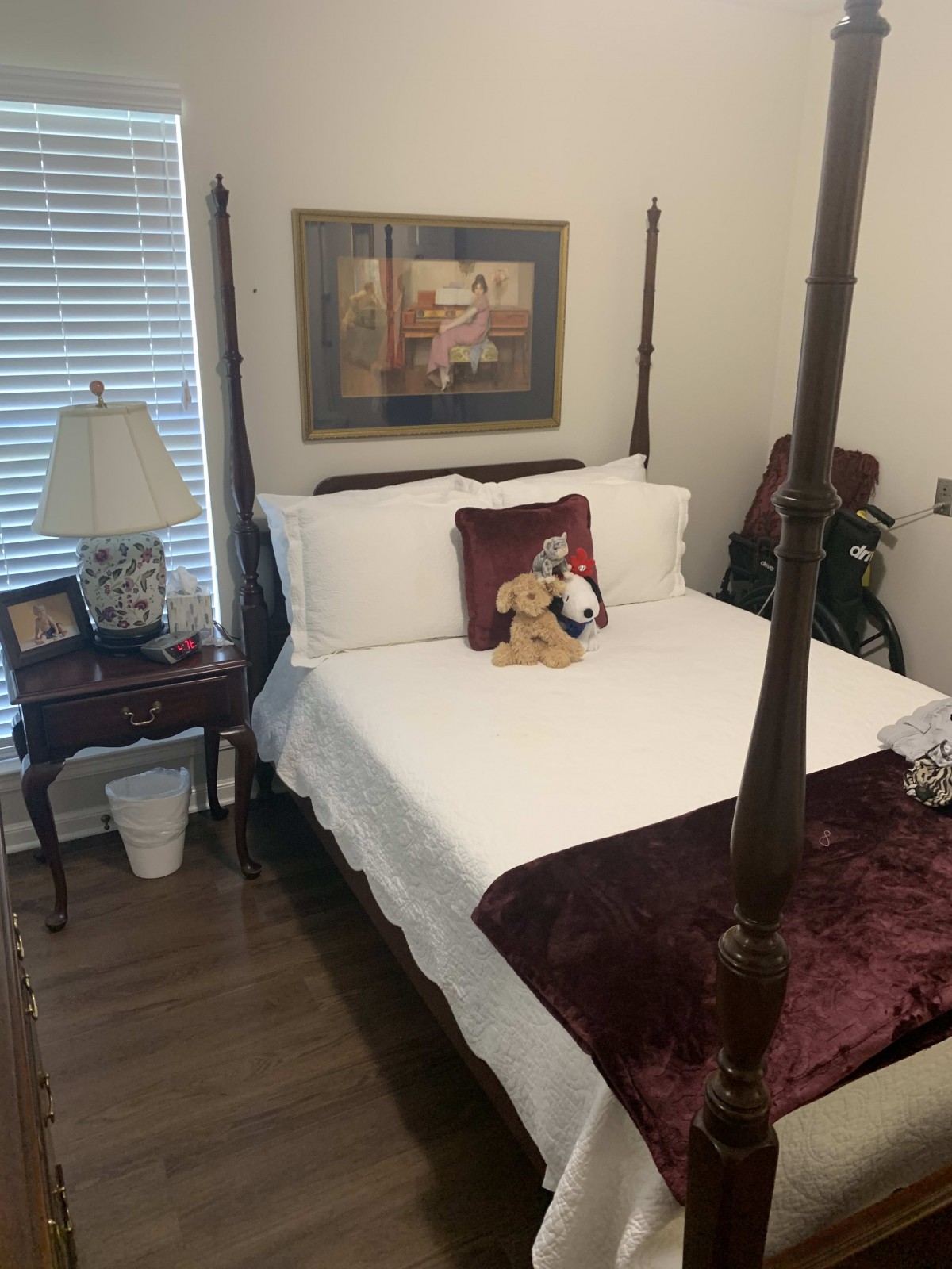A cozy bedroom featuring a four-poster bed with decorative pillows, a nightstand with a lamp, and a painting on the wall.