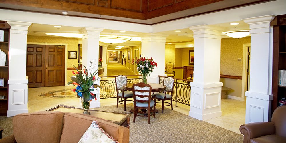 A cozy interior space featuring a small dining table with chairs, surrounded by floral arrangements and an elegant hallway.
