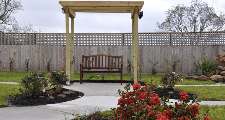 A serene garden scene with a wooden bench under a pergola, surrounded by colorful flowers.