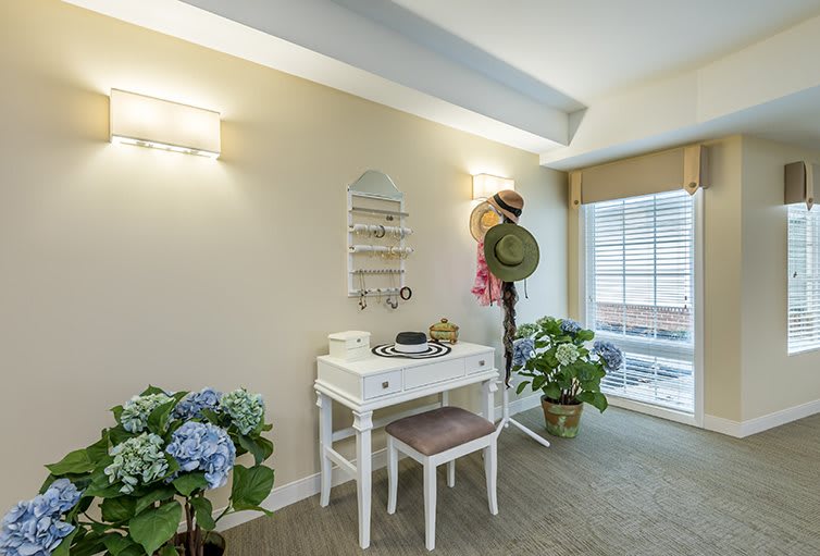 A well-decorated vanity area with a white makeup table, adorned with a mirror, hats, and floral accents.