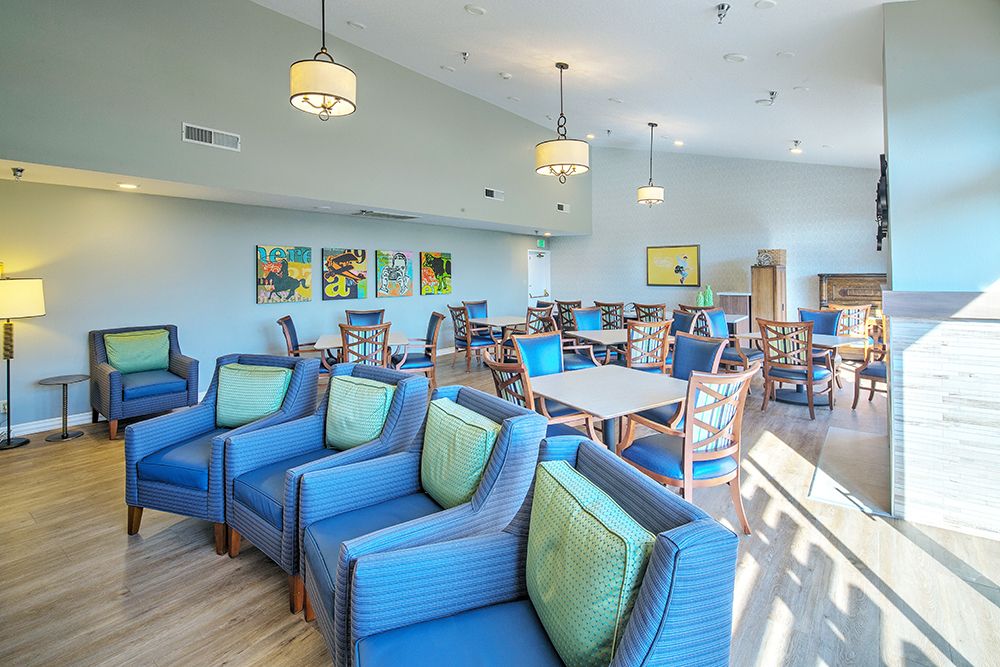 A spacious lounge area with blue upholstered chairs and tables, adorned with decorative lighting and artwork on the walls.