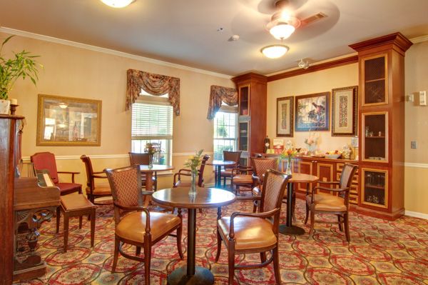 A cozy dining room with round tables and chairs arranged on a carpeted floor, featuring traditional decor.