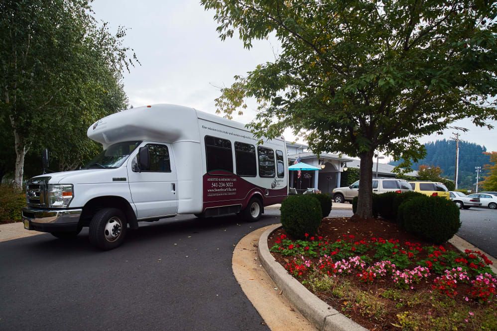 A shuttle bus parked in a lot surrounded by greenery and flowers.