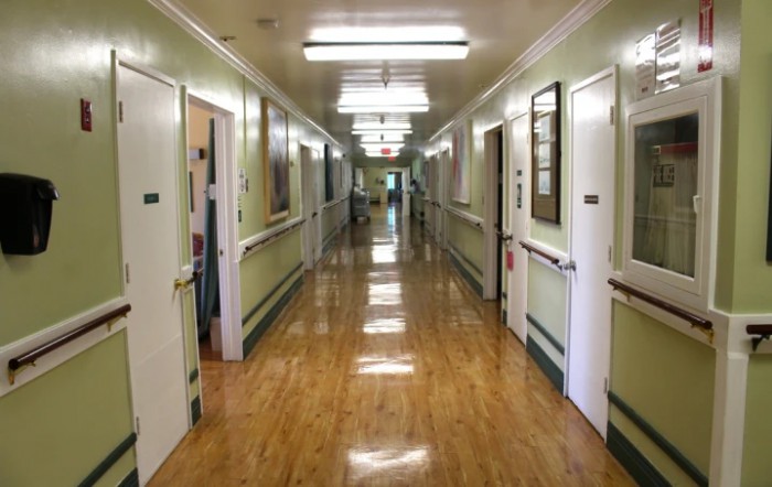 A quiet hospital corridor with multiple doors and bright overhead lighting.
