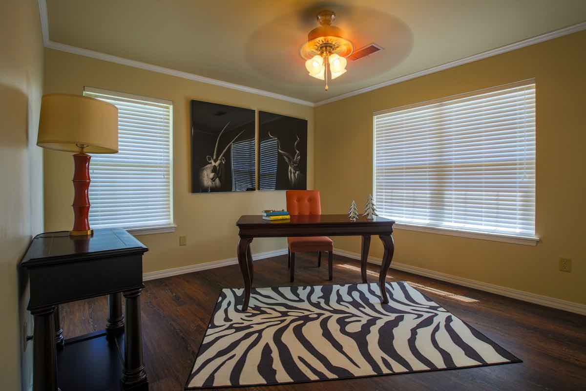A cozy home office with a wooden desk, zebra-print rug, and large windows allowing natural light.