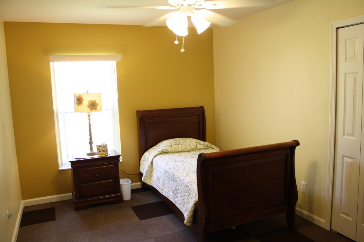 A cozy bedroom with a single wooden bed, nightstand, and a lamp near the window.