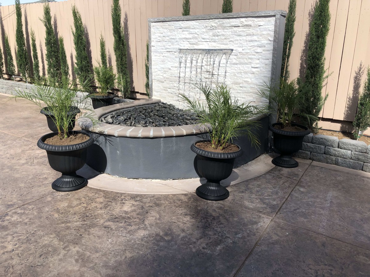 A modern garden fountain surrounded by potted plants in an outdoor setting.