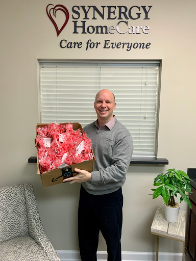 A cheerful man holding a box of gifts in an office setting.