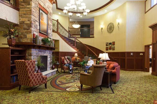 A cozy and inviting lobby featuring comfortable seating, a stone fireplace, and an elegant staircase.