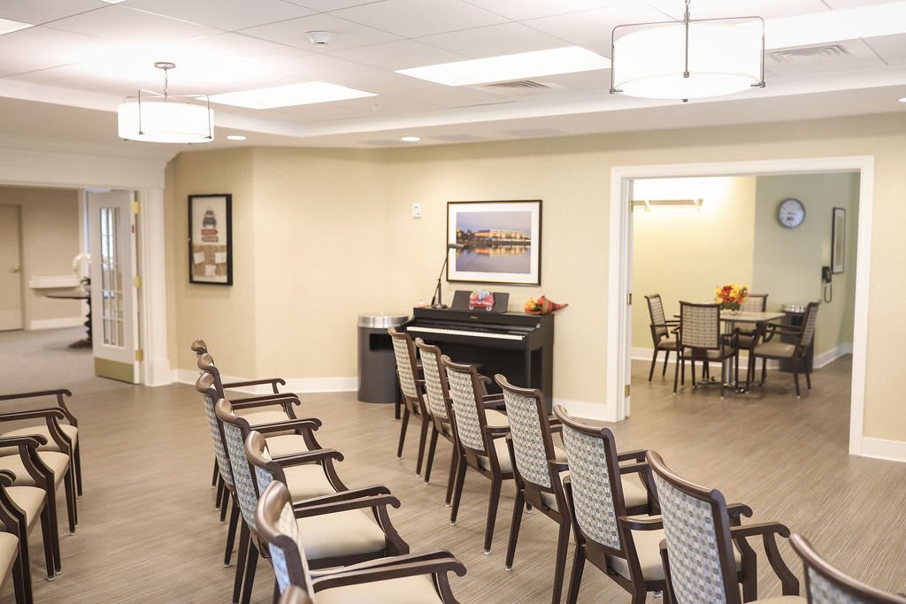 A conference room with neatly arranged chairs and a piano, featuring wall art and lighting fixtures.