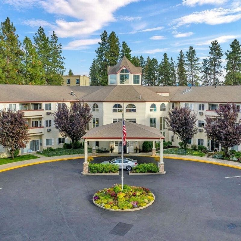 A spacious residential building with a circular driveway, surrounded by trees and landscaped gardens.