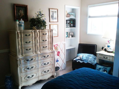 A cozy bedroom with a vintage dresser, artwork on the walls, and a comfortable chair in the corner.