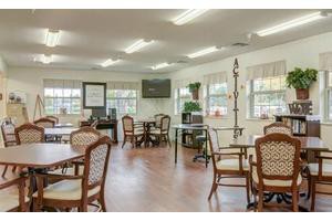 A well-lit community dining area with tables and chairs, featuring large windows and wood flooring.