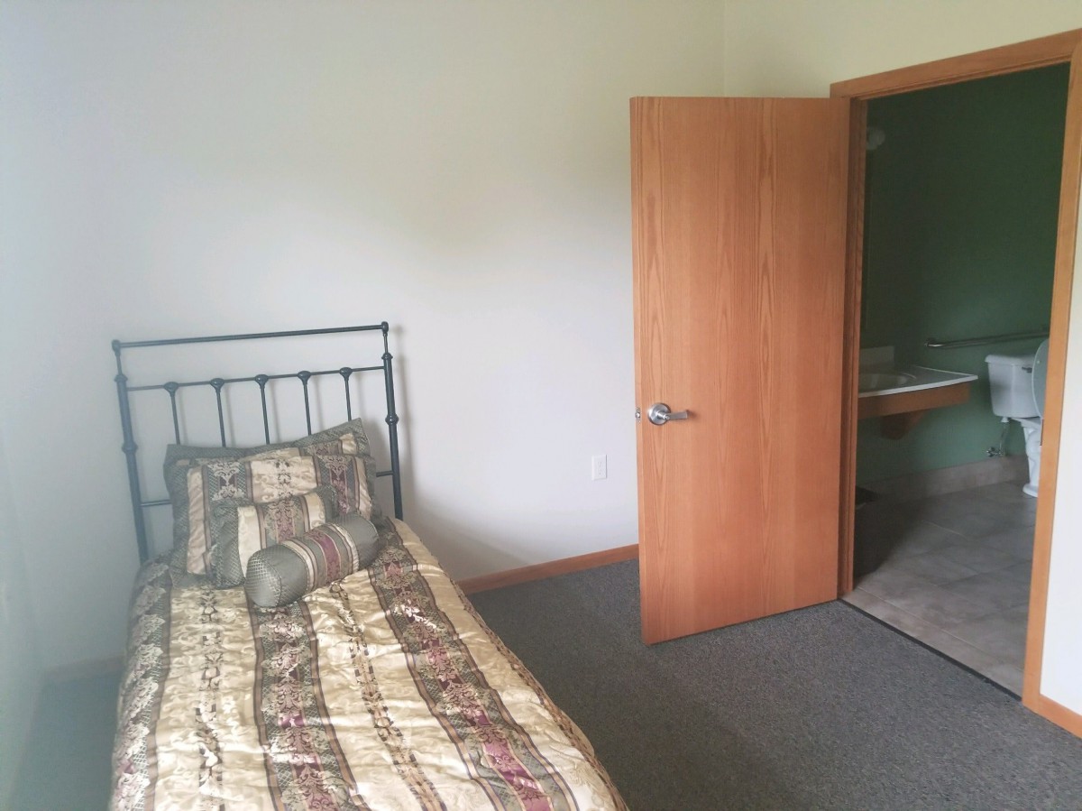 A simple bedroom with a single bed and an open door leading to another room.