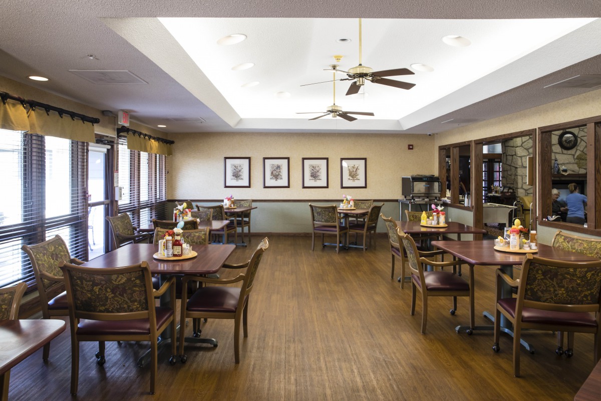 A neatly arranged dining room with wooden tables and chairs, ceiling fans, and framed artwork on the walls.