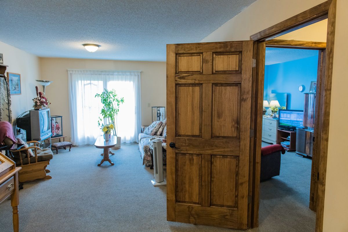 A cozy living room with wooden door, furniture, and a potted plant by the window.