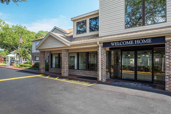 The entrance of a hotel building with a 'Welcome Home' sign on a sunny day.