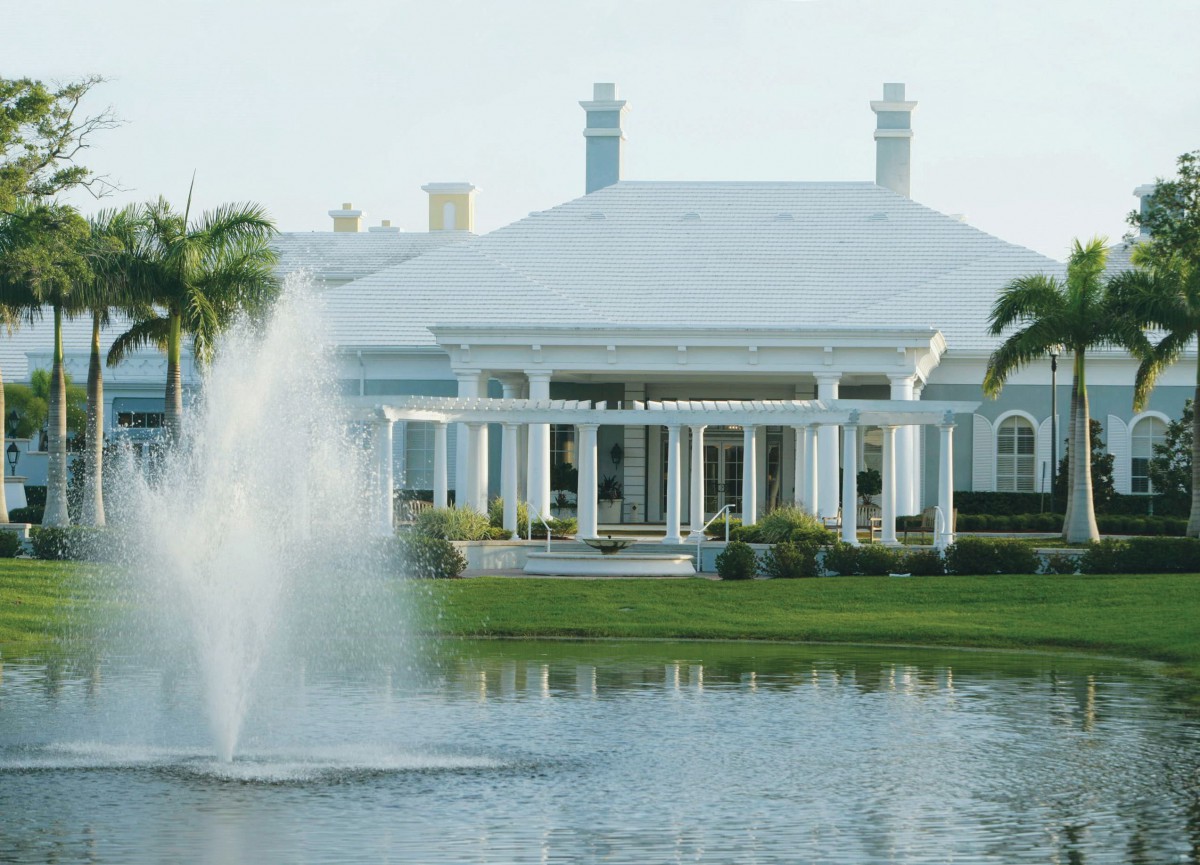 A picturesque view of a large building with white columns, surrounded by palm trees and a fountain in the foreground.