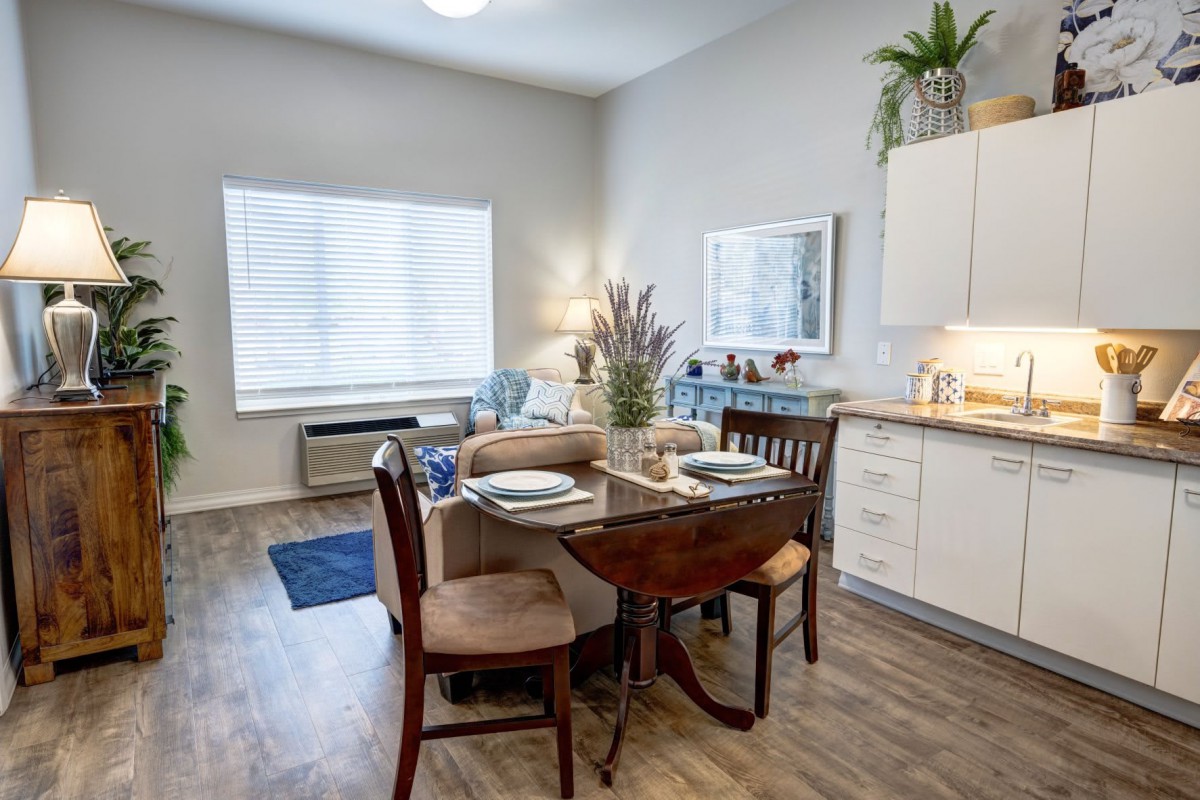 A cozy dining area with a wooden table set for two, adjacent to a compact kitchen.