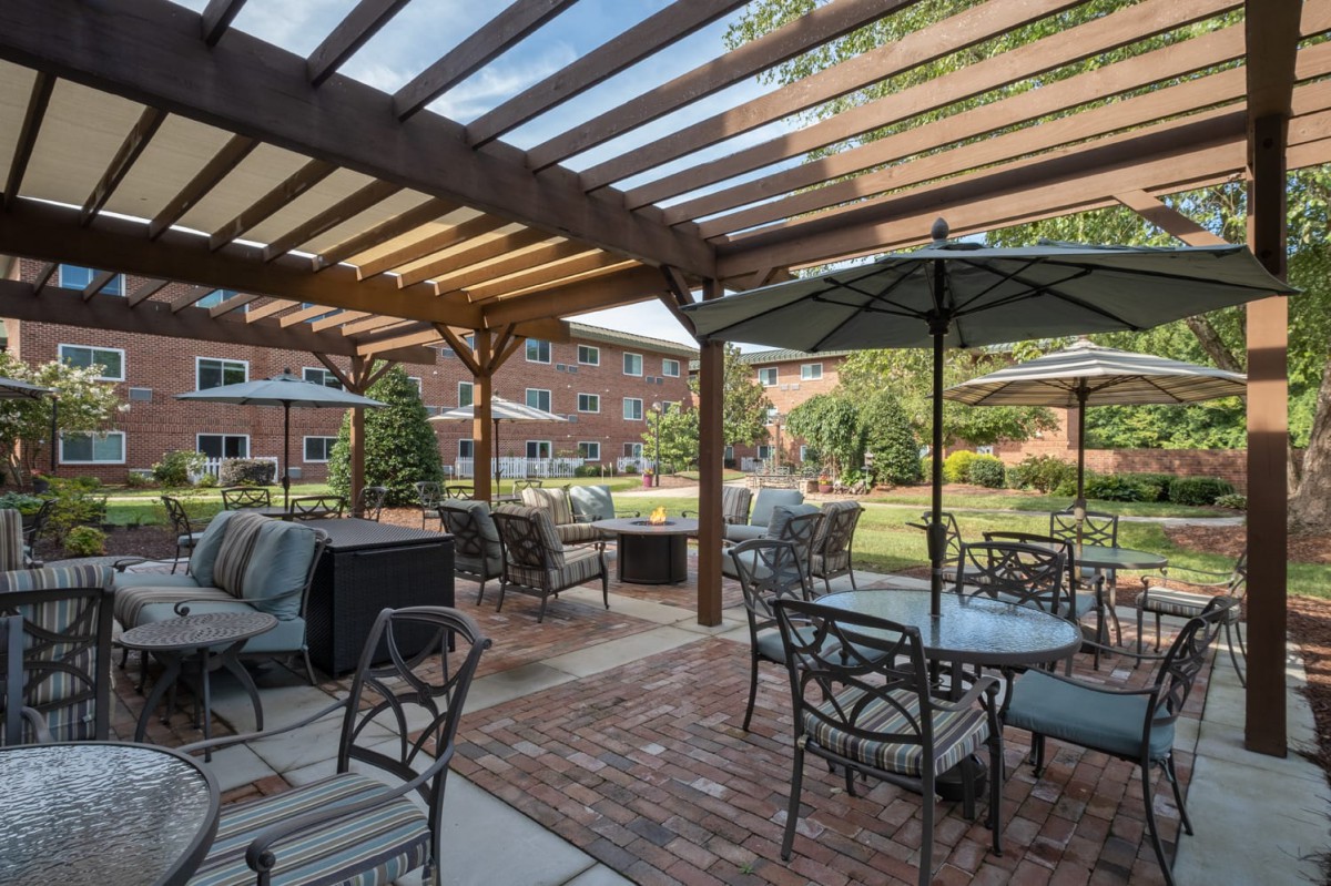 A tranquil outdoor patio area featuring tables, chairs, and a pergola with views of a garden.
