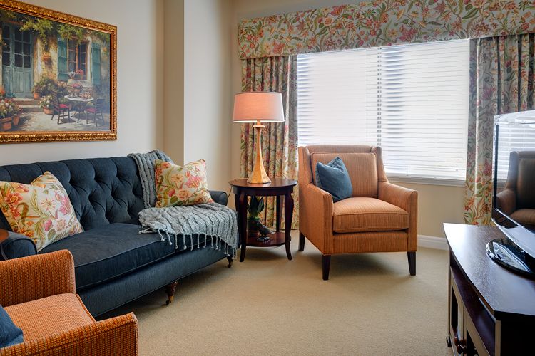 A cozy living room with a sofa, armchair, and lamp by the window.