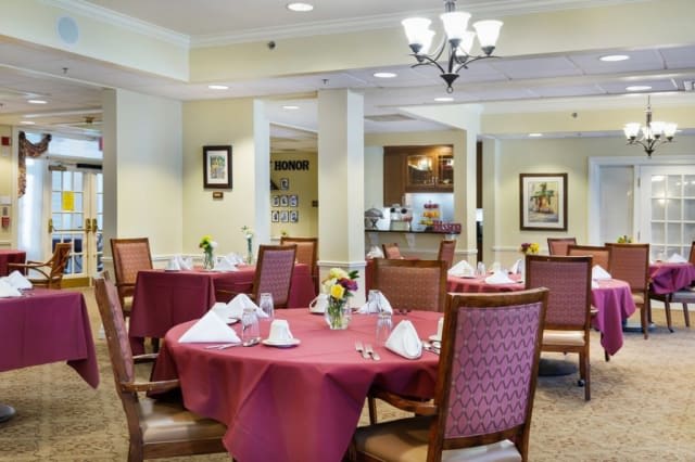 A well-set dining room with tables and chairs, featuring elegant table settings and a chandelier.