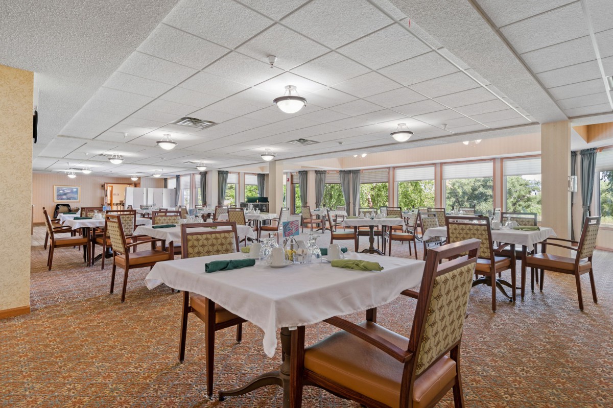 A spacious restaurant dining area with neatly arranged tables and chairs, featuring large windows that allow natural light to fill the room.