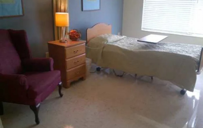 A cozy bedroom with a single bed, nightstand with a lamp, and a comfortable chair.