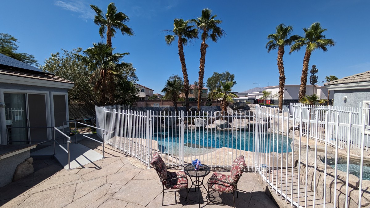 A sunny outdoor area featuring a swimming pool surrounded by palm trees and patio furniture.