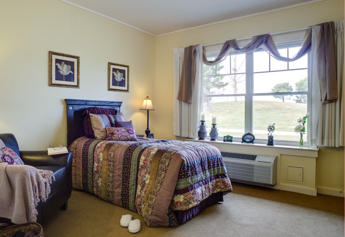 A cozy bedroom with a single bed, bedside lamp, and a large window providing natural light.