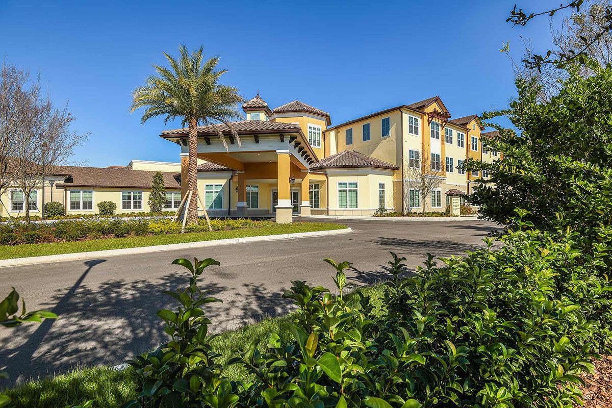 A sunny day highlights a modern architectural building with palm trees at the entrance.