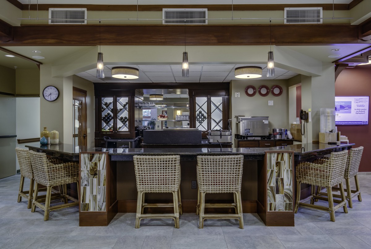 A modern bar interior with woven chairs and wine racks behind the counter.