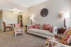 A cozy living room featuring a sofa with pink cushions, floral chairs, and elegant lighting.