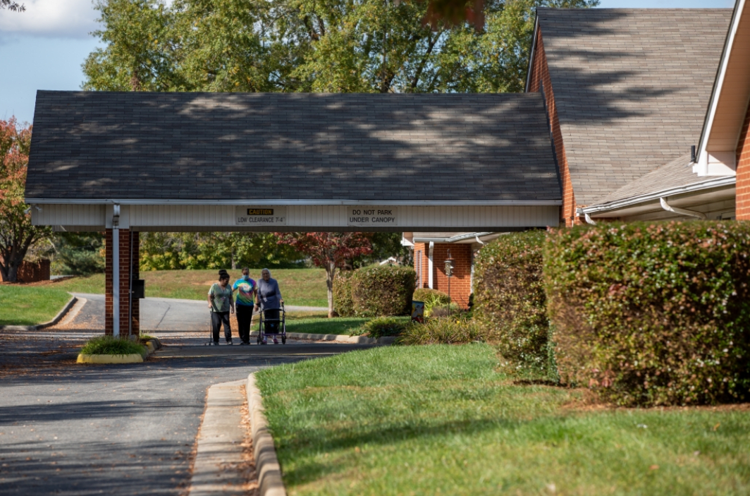 Three people standing on a driveway near a residential building.