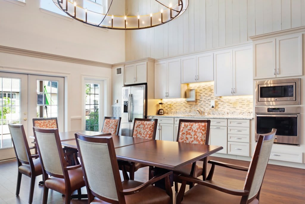A modern kitchen and dining area featuring a large wooden table, comfortable chairs, white cabinets, and a stylish chandelier.