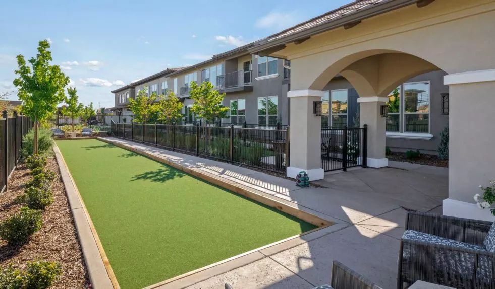 A residential complex with a bocce ball court and manicured landscaping under a clear blue sky.
