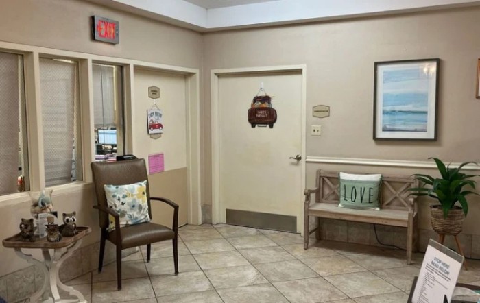 A cozy waiting room with chairs and decorative pillows, featuring signs and a closed door.