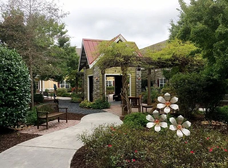 A serene garden pathway leading to a small building surrounded by lush greenery and flowers.