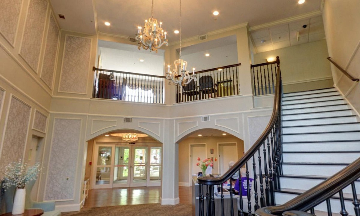 A grand foyer with a chandelier, curved staircase, and upper-level balcony.