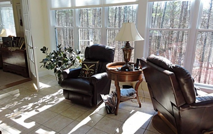 A cozy living room area with two chairs, a lamp on a side table, and sunlight streaming through large windows.