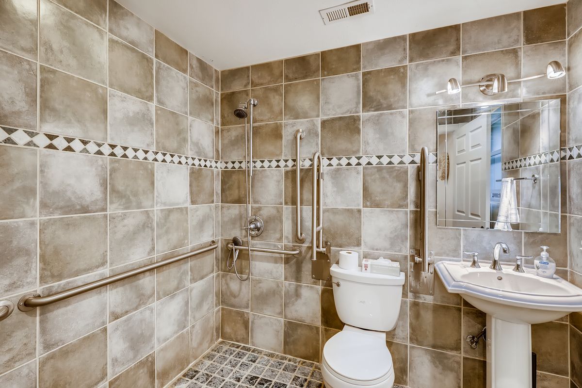 An accessible bathroom with tiled walls and floor, featuring a toilet, sink, and grab bars.