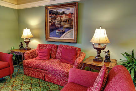 A cozy living room with a red patterned sofa, elegant lamps, and a painting on the wall.