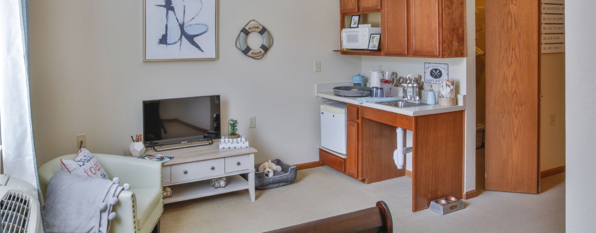 A cozy apartment kitchen with wooden cabinets and a small living area.