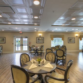 A well-lit dining room with round tables and elegant chairs set on a wooden floor.