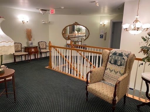 A cozy hallway with traditional decor, featuring an armchair, mirror, and wood railing.