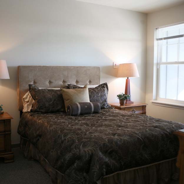 A cozy bedroom with a neatly made bed, flanked by bedside tables and lamps, with natural light streaming in through the window.