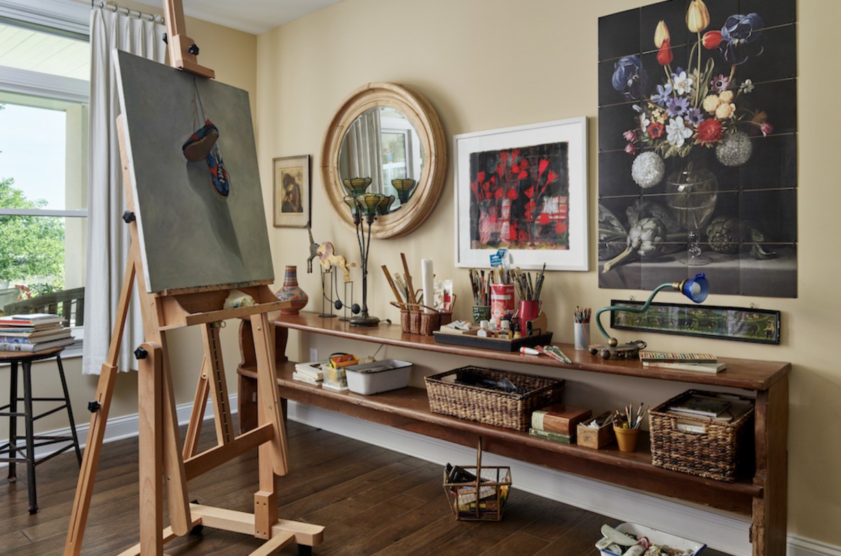 A cozy art studio featuring an easel, shelves lined with art supplies, and several paintings on display.