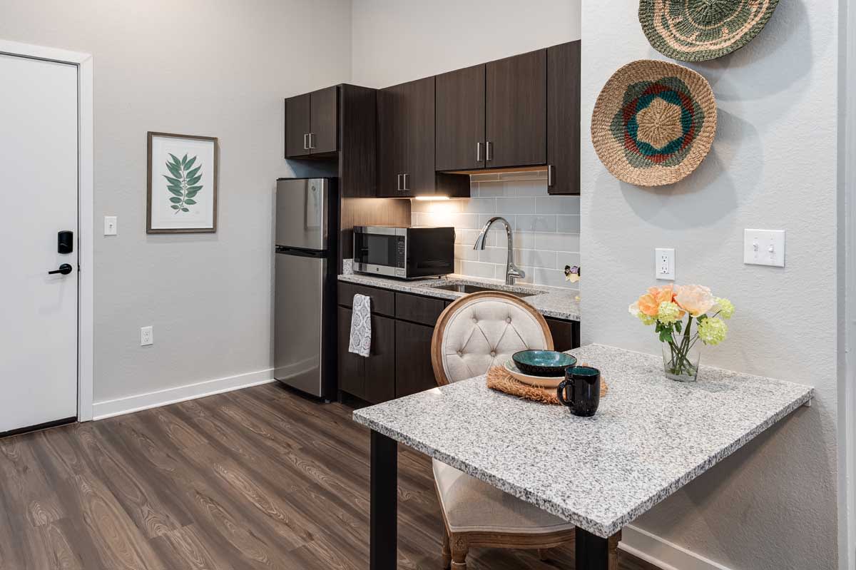 A modern kitchen with a small dining area, featuring dark wood cabinets, stainless steel appliances, and a granite countertop.